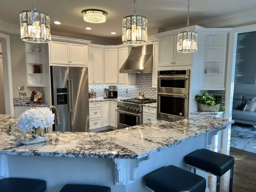 A kitchen with freshly painted white cabinets, a granite island and pendant lighting