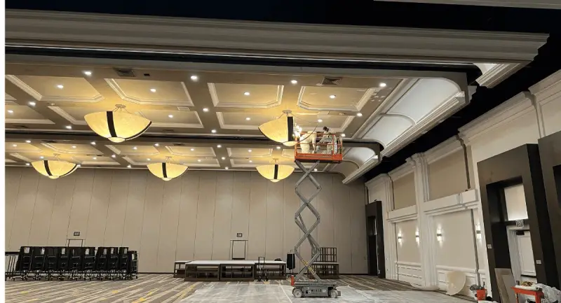 A painter on a scissor lift working across the coffered ceiling of a large event space