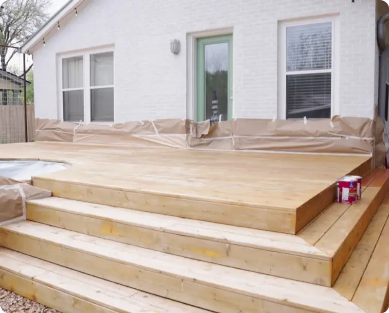Freshly stained cedar deck steps with the surrounding area masked off during the job