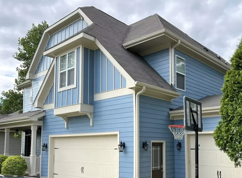 A blue board and batten home with white trim and a repainted garage