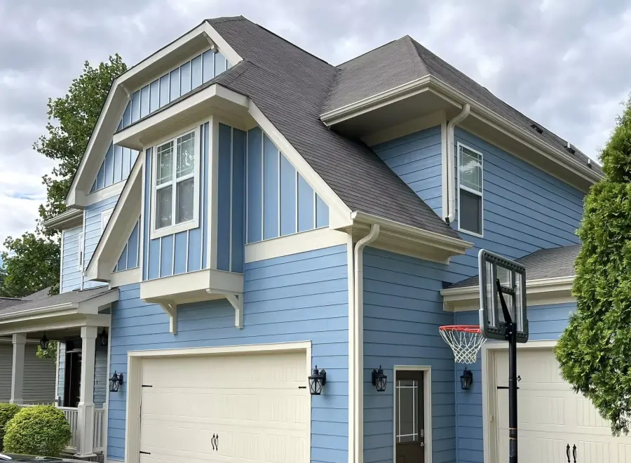 A blue board and batten home with white trim and a repainted garage
