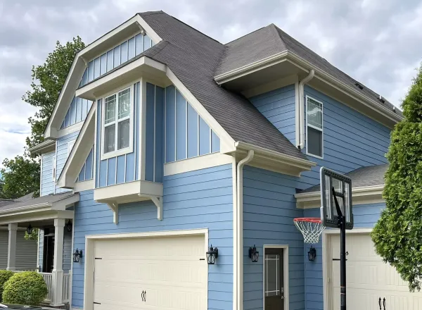 A blue board and batten home with white trim and a repainted garage