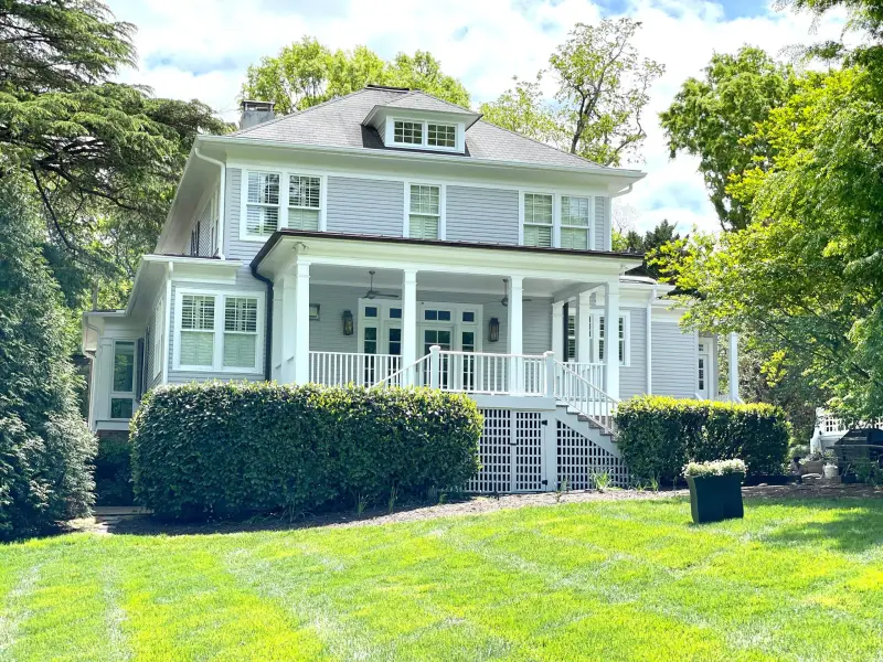 A pale green two-story home with a white front porch and freshly painted trim