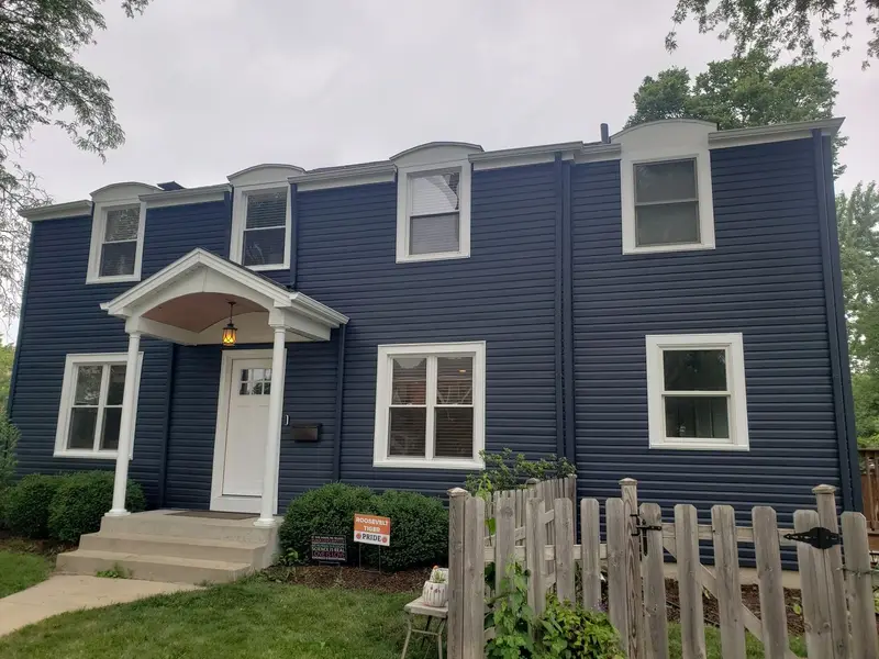 A navy clapboard colonial with white window trim, a white portico and a picket fence