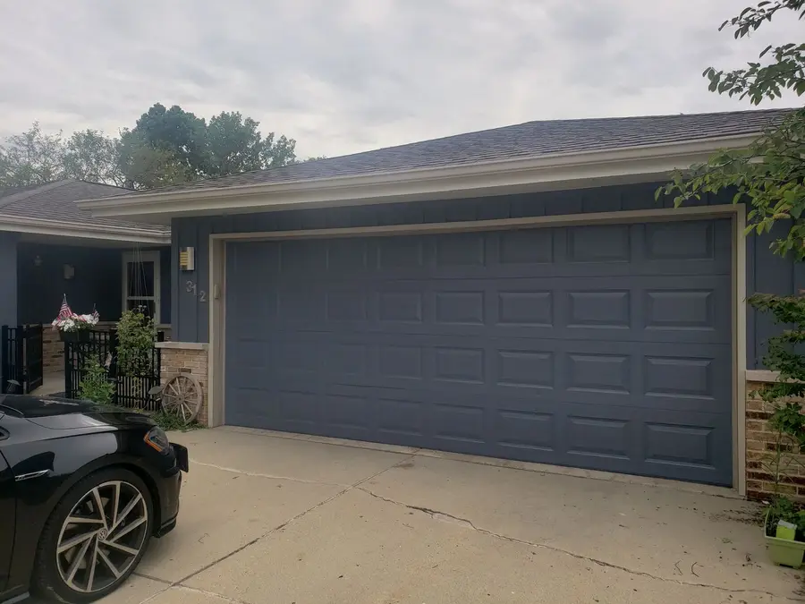 A ranch home with dark navy siding and a repainted navy garage door above a concrete drive
