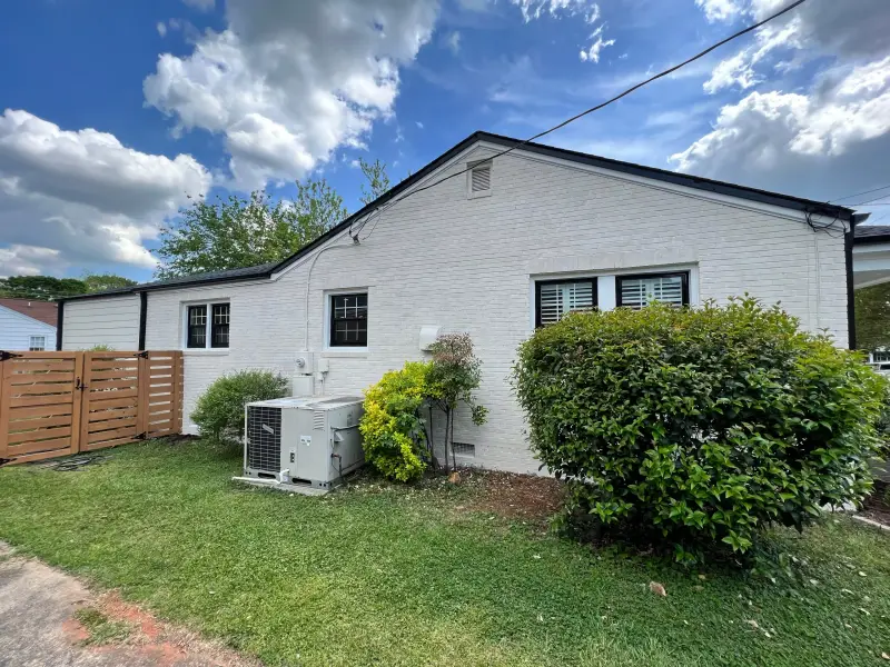 A white painted brick ranch home with dark window frames and trimmed hedges
