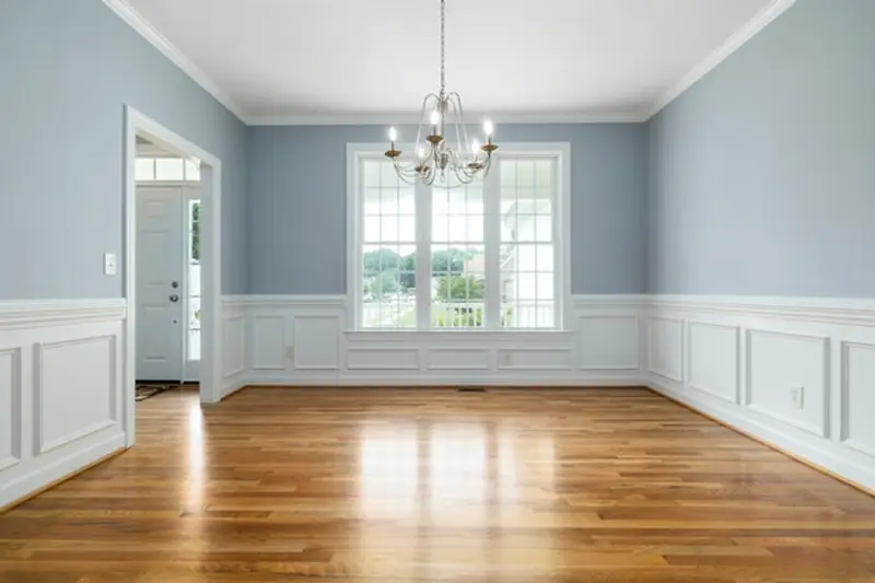 A dining room with soft blue walls, white wainscoting and a chandelier