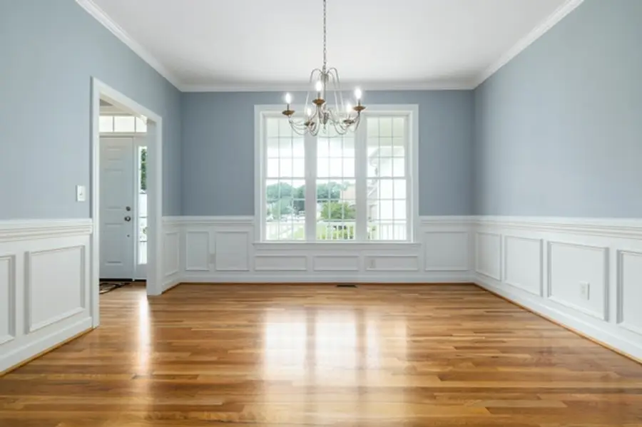 A dining room with soft blue walls, white wainscoting and a chandelier