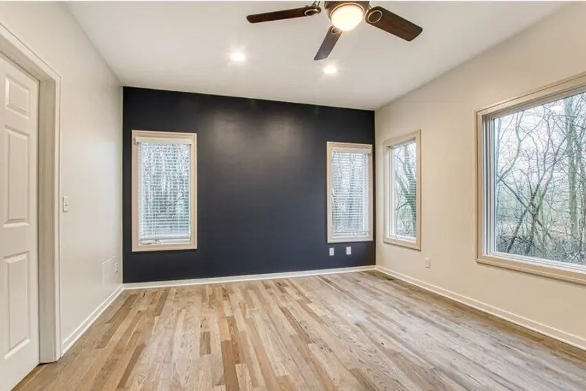 A living room with a navy accent wall between two windows and pale walls on the return