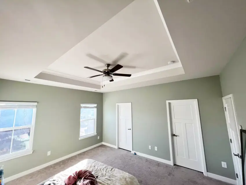 A bedroom painted in a soft sage green with white doors and trim