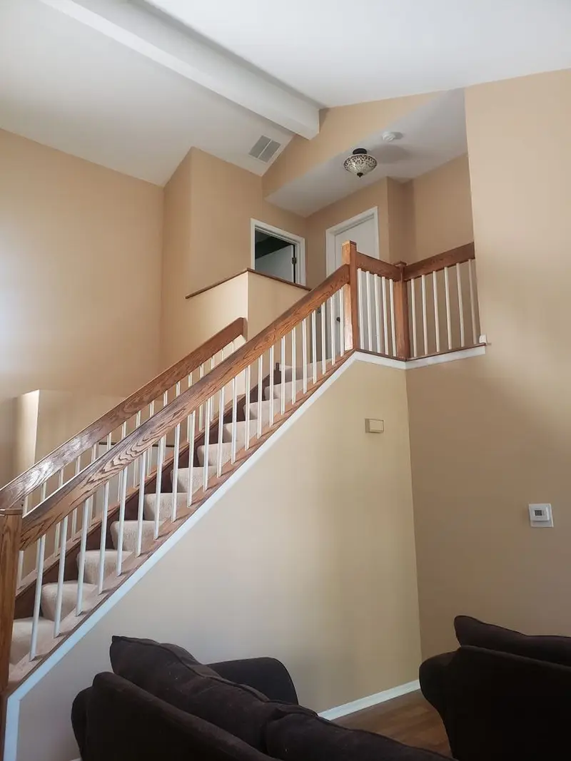 A stair hall painted in a warm tan with a white spindle railing and an oak handrail