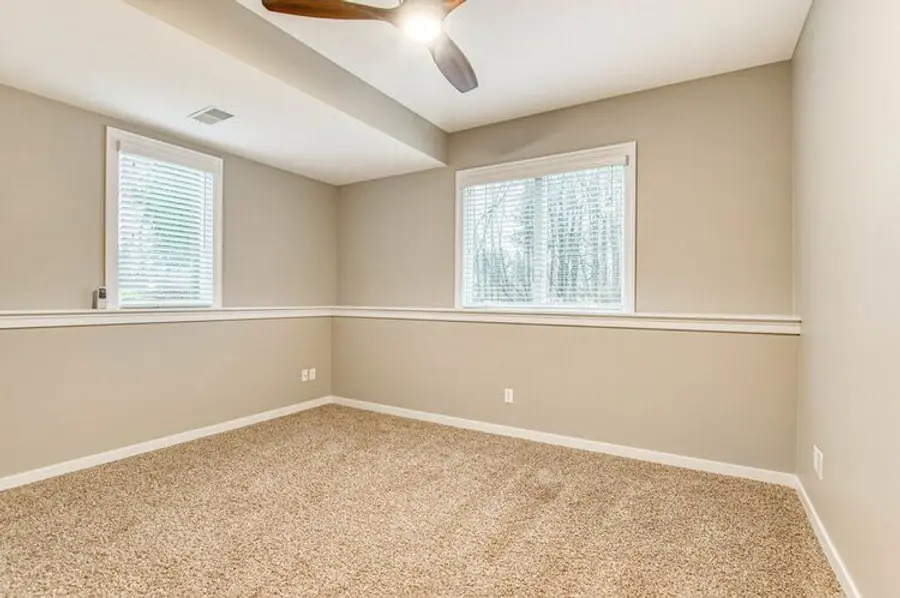 An empty room painted in a warm tan above and below a white chair rail, with a ceiling fan