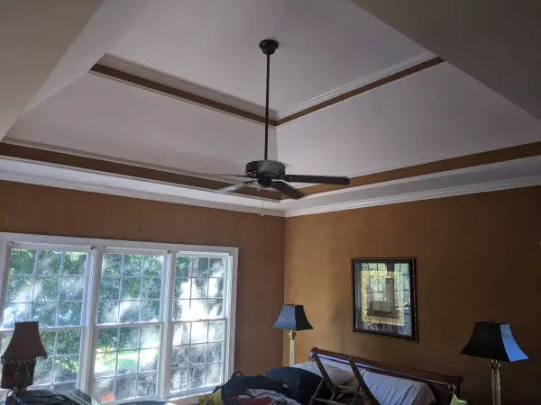 A bedroom with warm toned walls and a white tray ceiling